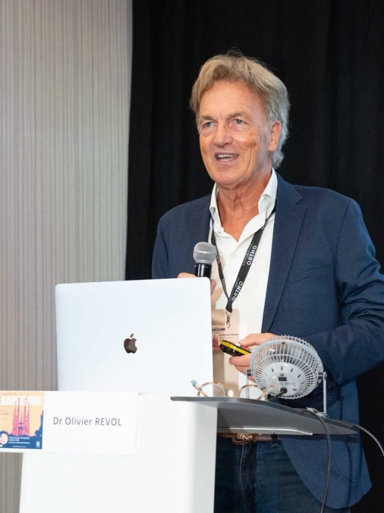 Le Dr Olivier Revol au pupitre, micro à la main, devant un rideau noir, pendant sa conférence au congrès de la SBR à Barcelone, le 2 octobre 2026